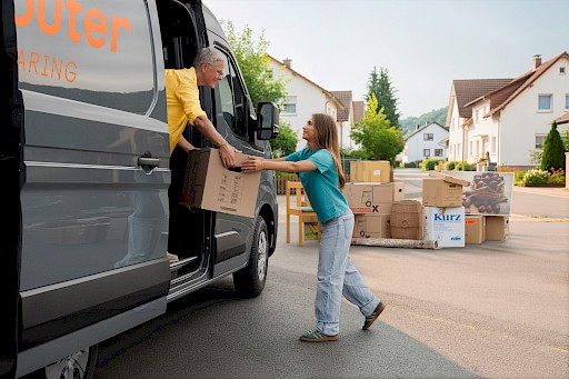 Eine ältere Frau in einem Transporter nimmt eine Umzugskiste von einer jungen Frau entgegen.